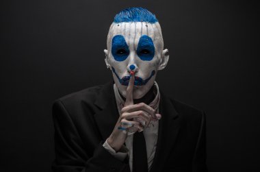 Terrible clown and Halloween theme: Crazy blue clown in black suit isolated on a dark background in the studio
