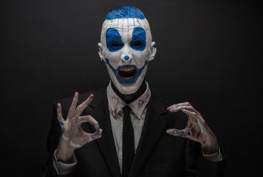 Terrible clown and Halloween theme: Crazy blue clown in black suit isolated on a dark background in the studio