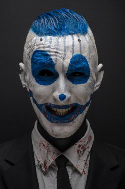 Terrible clown and Halloween theme: Crazy blue clown in black suit isolated on a dark background in the studio