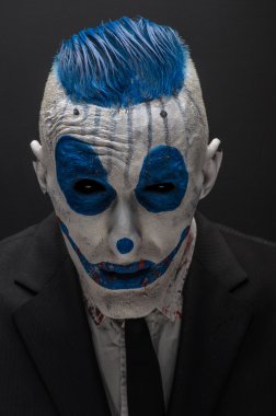 Terrible clown and Halloween theme: Crazy blue clown in black suit isolated on a dark background in the studio