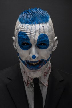 Terrible clown and Halloween theme: Crazy blue clown in black suit isolated on a dark background in the studio