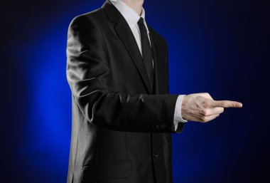 Business and the presentation of the theme: man in a black suit showing hand gestures on a dark blue background in studio isolated