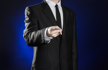 Business and the presentation of the theme: man in a black suit showing hand gestures on a dark blue background in studio isolated