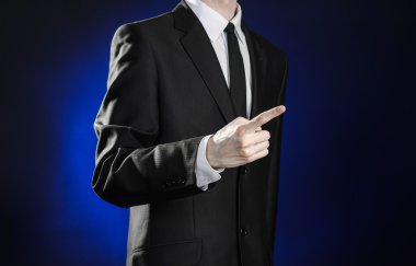 Business and the presentation of the theme: man in a black suit showing hand gestures on a dark blue background in studio isolated