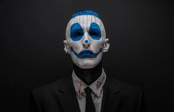 Terribile clown e tema Halloween: clown blu pazzo in abito nero isolato su uno sfondo scuro in studio — Foto Stock