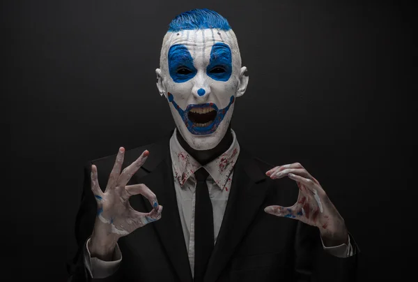 Terribile clown e tema Halloween: clown blu pazzo in abito nero isolato su uno sfondo scuro in studio — Foto Stock