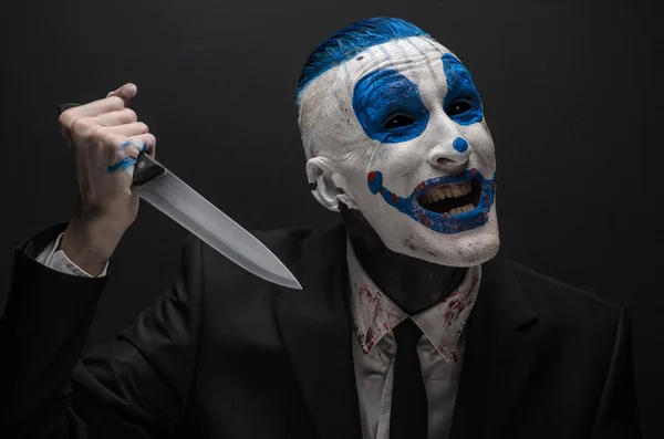 Terrible clown and Halloween theme: Crazy blue clown in a black suit with a knife in his hand isolated on a dark background in the studio — Stockfoto