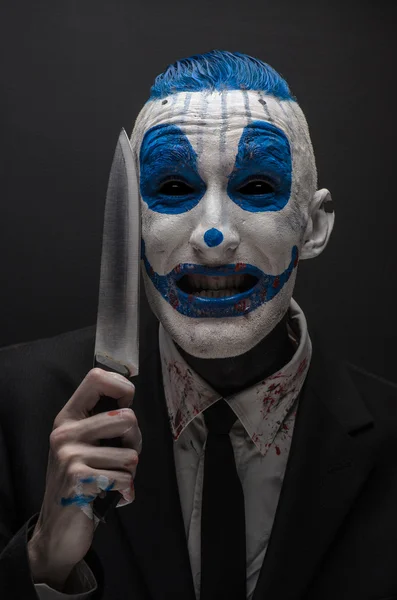 Terrible clown and Halloween theme: Crazy blue clown in a black suit with a knife in his hand isolated on a dark background in the studio — Stok fotoğraf