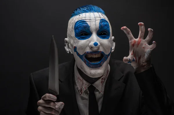 Terrible clown and Halloween theme: Crazy blue clown in a black suit with a knife in his hand isolated on a dark background in the studio — Stok fotoğraf