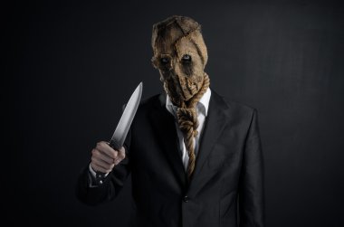 Fear and Halloween theme: a brutal killer in a mask holding a knife on a dark background in the studio
