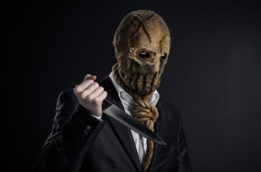 Fear and Halloween theme: a brutal killer in a mask holding a knife on a dark background in the studio