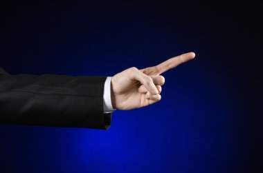 Businessman and gesture topic: a man in a black suit and white shirt showing hand gesture on an isolated dark blue background in studio