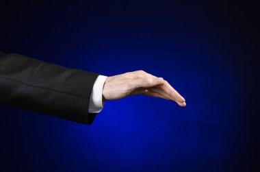 Businessman and gesture topic: a man in a black suit and white shirt showing hand gesture on an isolated dark blue background in studio
