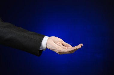 Businessman and gesture topic: a man in a black suit and white shirt showing hand gesture on an isolated dark blue background in studio