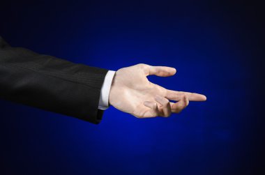 Businessman and gesture topic: a man in a black suit and white shirt showing hand gesture on an isolated dark blue background in studio