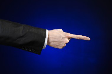 Businessman and gesture topic: a man in a black suit and white shirt showing hand gesture on an isolated dark blue background in studio