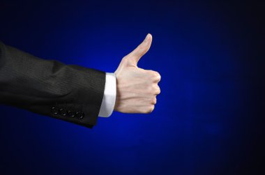 Businessman and gesture topic: a man in a black suit and white shirt showing hand gesture on an isolated dark blue background in studio