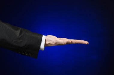 Businessman and gesture topic: a man in a black suit and white shirt showing hand gesture on an isolated dark blue background in studio