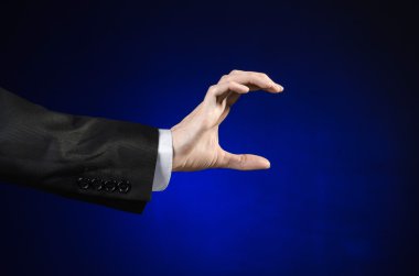 Businessman and gesture topic: a man in a black suit and white shirt showing hand gesture on an isolated dark blue background in studio