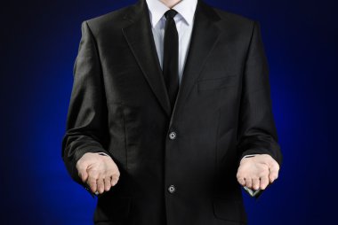 Businessman and gesture topic: a man in a black suit and white shirt showing gestures with hands on a dark blue background in studio isolated