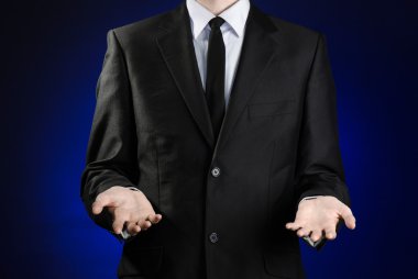 Businessman and gesture topic: a man in a black suit and white shirt showing gestures with hands on a dark blue background in studio isolated