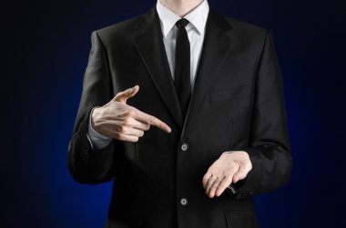 Businessman and gesture topic: a man in a black suit and white shirt showing gestures with hands on a dark blue background in studio isolated