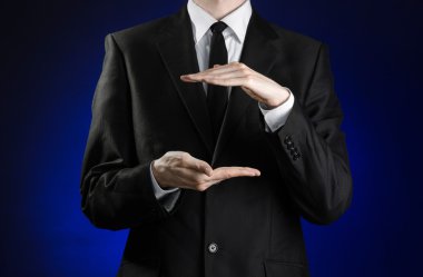 Businessman and gesture topic: a man in a black suit and white shirt showing gestures with hands on a dark blue background in studio isolated