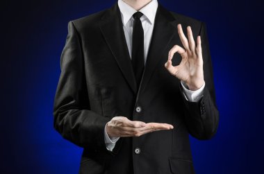 Businessman and gesture topic: a man in a black suit and white shirt showing gestures with hands on a dark blue background in studio isolated