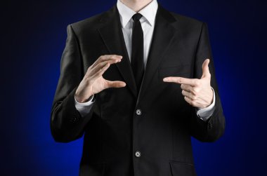 Businessman and gesture topic: a man in a black suit and white shirt showing gestures with hands on a dark blue background in studio isolated