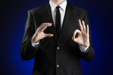 Businessman and gesture topic: a man in a black suit and white shirt showing gestures with hands on a dark blue background in studio isolated