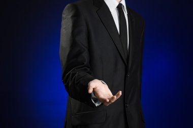 Businessman and gesture topic: a man in a black suit and white shirt holds up a hand against the dark blue isolated background in studio