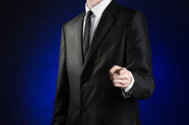Businessman and gesture topic: a man in a black suit and white shirt shows his hand forward on a dark blue background in studio isolated