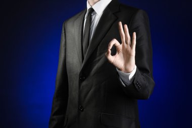 Businessman and gesture topic: a man in a black suit and white shirt showing okay hand sign on a dark blue background in studio isolated