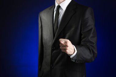 Businessman and gesture topic: a man in a black suit and white shirt showing fig hand on a dark blue background in studio isolated