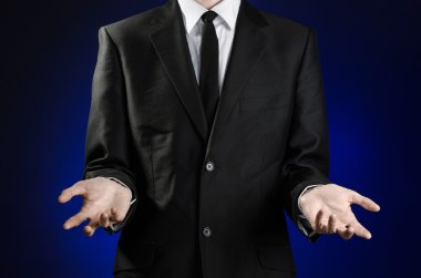 Businessman and gesture topic: a man in a black suit and white shirt showing gestures with hands on a dark blue background in studio isolated