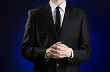 Businessman and gesture topic: a man in a black suit and white shirt holds her hands together in front of you and prays, meditates on a dark blue background in studio isolated