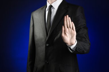Businessman and gesture topic: a man in a black suit and white shirt shows a hand stop sign on a dark blue background in studio isolated