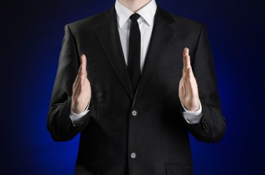 Businessman and gesture topic: a man in a black suit and white shirt showing gestures with hands on a dark blue background in studio isolated