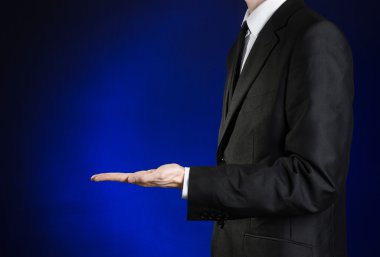 Businessman and gesture topic: a man in a black suit and white shirt showing gestures with hands on a dark blue background in studio isolated