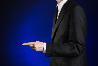 Businessman and gesture topic: a man in a black suit and white shirt shows his hand forward on a dark blue background in studio isolated