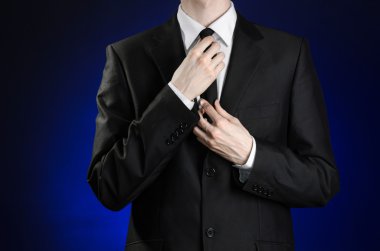 Businessman and gesture topic: a man in a black suit and white shirt correcting a jacket and tie on a dark blue background in studio isolated