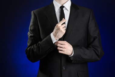 Businessman and gesture topic: a man in a black suit and white shirt correcting a jacket and tie on a dark blue background in studio isolated