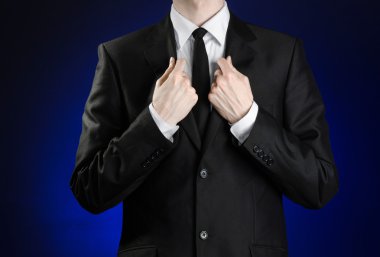 Businessman and gesture topic: a man in a black suit and white shirt correcting a jacket and tie on a dark blue background in studio isolated