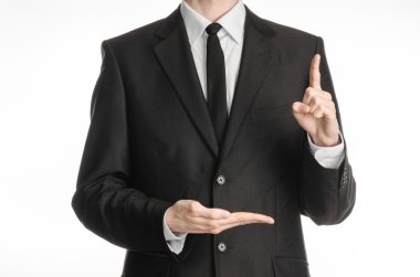 Businessman and gesture topic: a man in a black suit with a tie shows the left hand index finger up and keeps his right hand on a white isolated background in studio