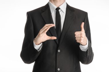 Businessman and gesture topic: a man in a black suit and tie holds his right hand and the left shows a thumb-up sign isolated on white background in studio
