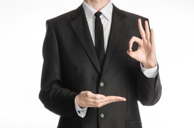 Businessman and gesture topic: a man in a black suit with a tie showing okay sign with his left hand and holds his right hand on a white isolated background in studio