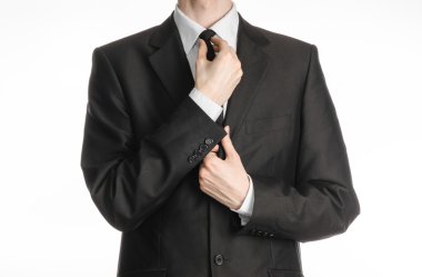 Businessman and gesture topic: a man in a black suit with a tie straightens his tie isolated on white background in studio