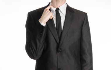 Businessman and gesture topic: a man in a black suit and tie holding a hand to his shirt collar isolated on a white background in studio
