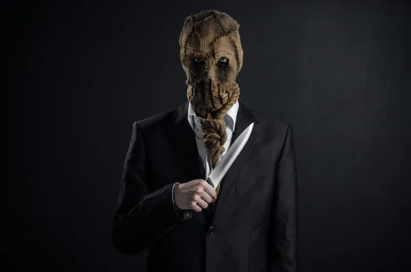 Fear and Halloween theme: a brutal killer in a mask holding a knife on a dark background in the studio — Stock Photo, Image