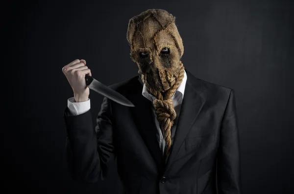 Fear and Halloween theme: a brutal killer in a mask holding a knife on a dark background in the studio — Stock Photo, Image